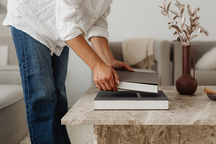 A woman stacking books on a table at home.