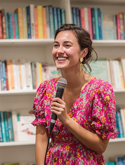 A young female author in a bright pink dress speaking at a book store event.